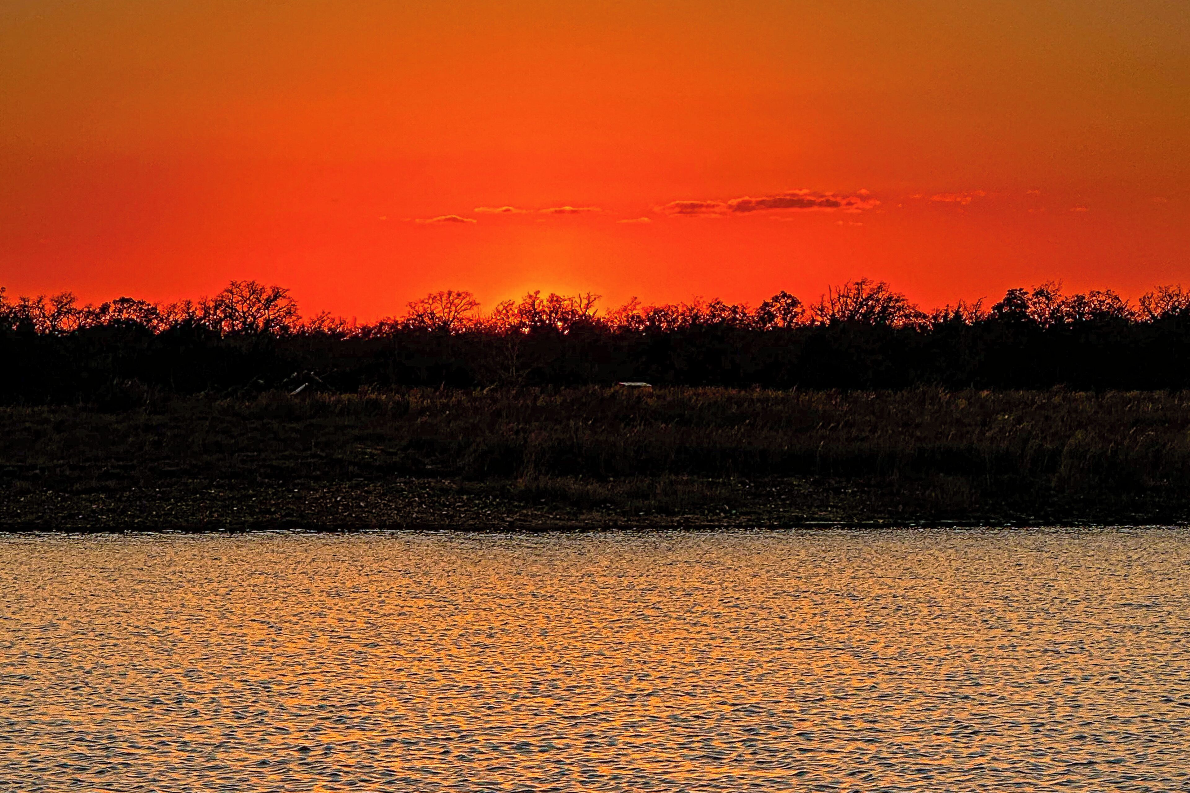 A sunset over a body of water with a silhouette of trees in the background.