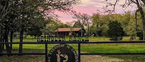 A sign with the text "REINDEER RANCH" and "EVERYDAY IS CHRISTMAS" in a rural setting with trees and a building in the background.