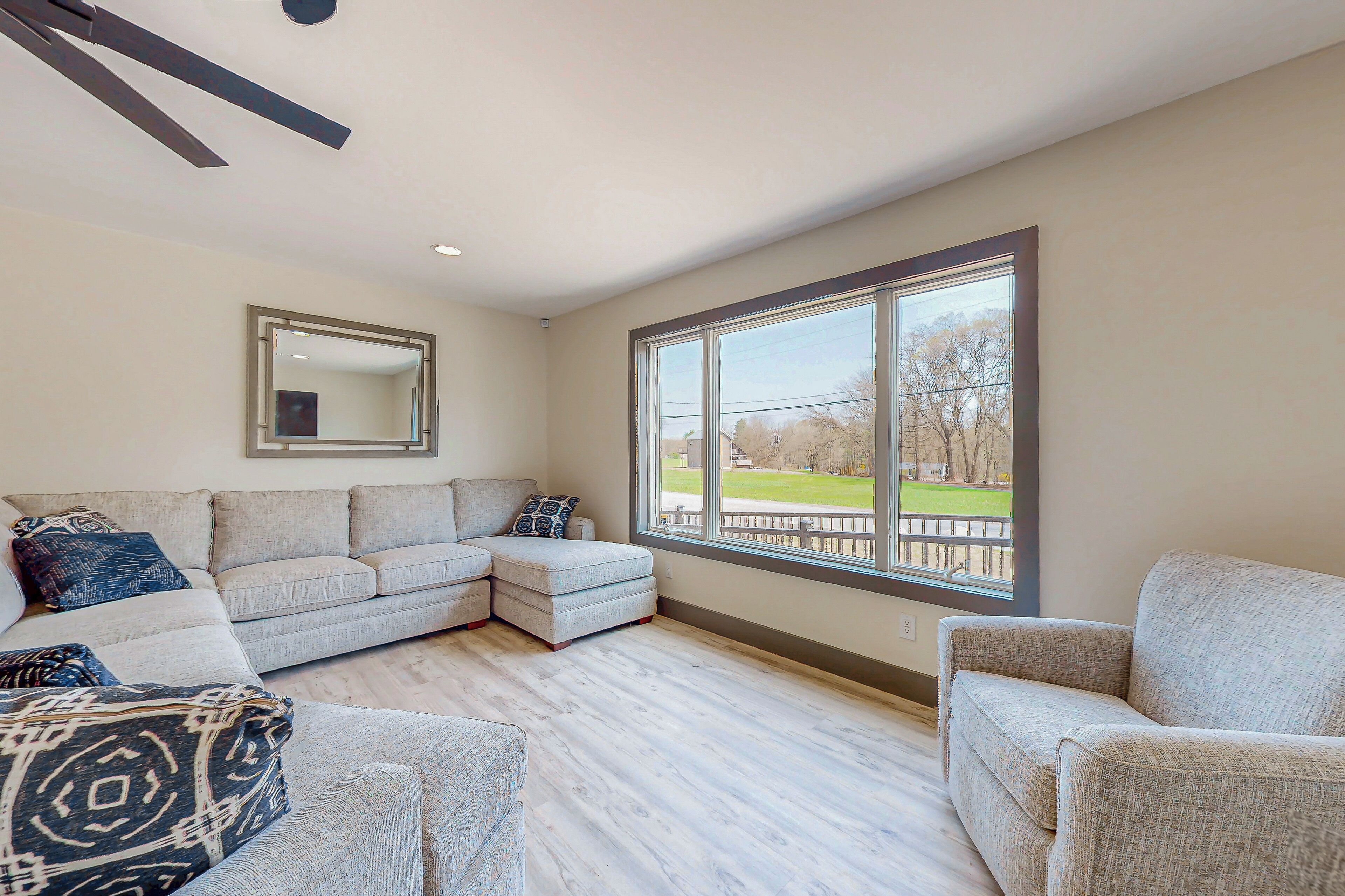 A living room with a sectional sofa, a small loveseat, and a large window offering a view of a park.