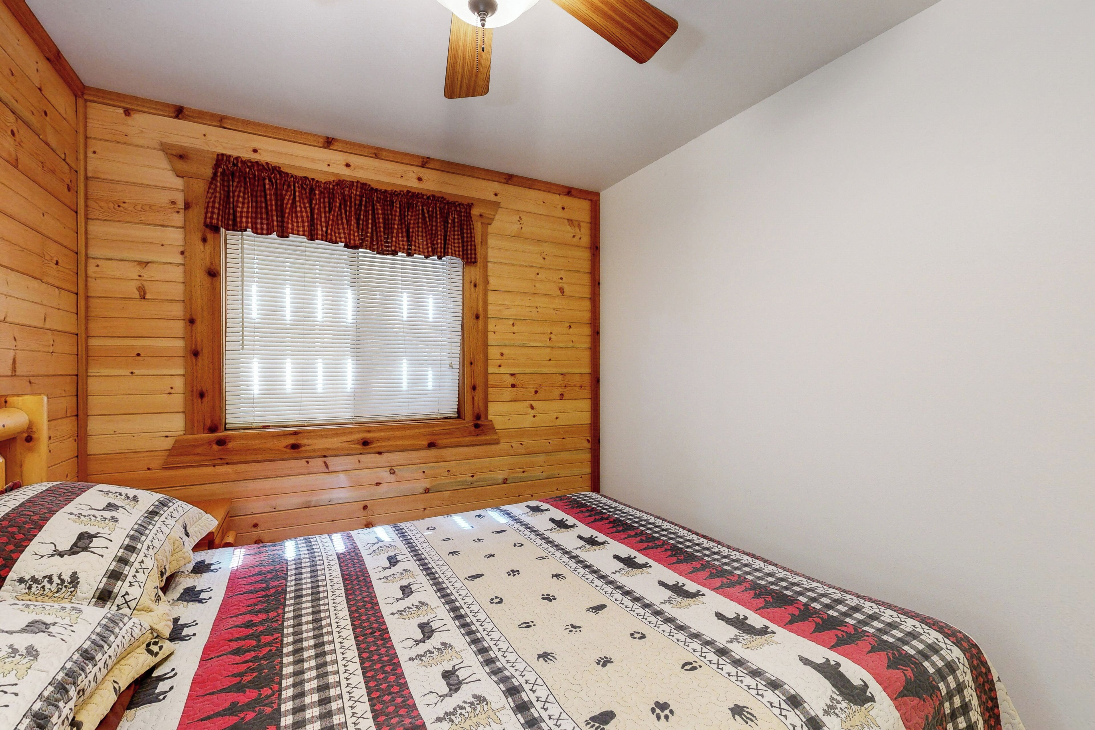 A wooden-paneled room with a bed, a window with blinds, and a ceiling fan.