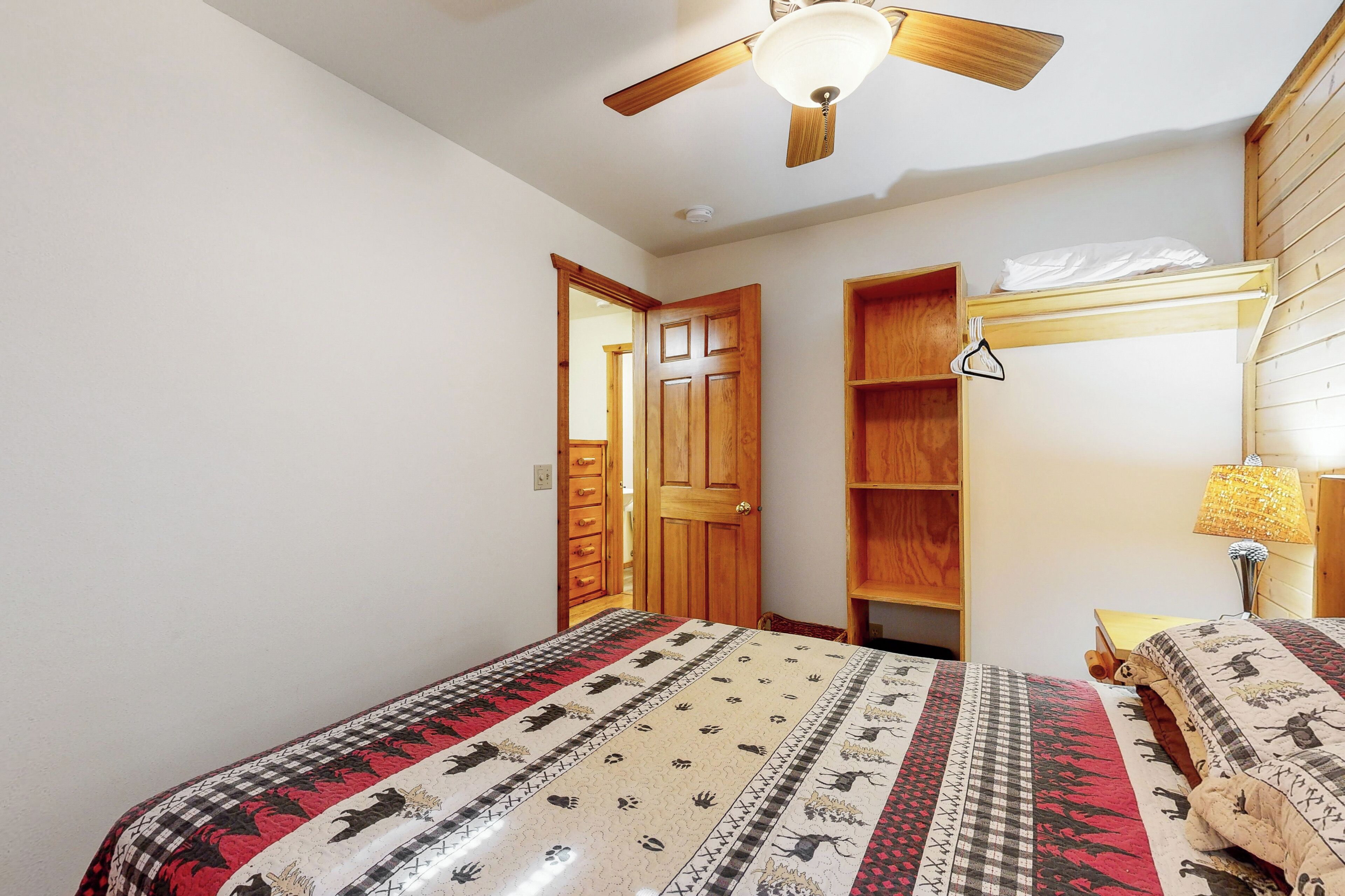 A bedroom with a bed, a ceiling fan, a wooden door, and a nightstand with a lamp.