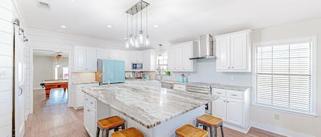 A spacious kitchen with white cabinetry, a large island with stools, and a view of the adjacent living area.