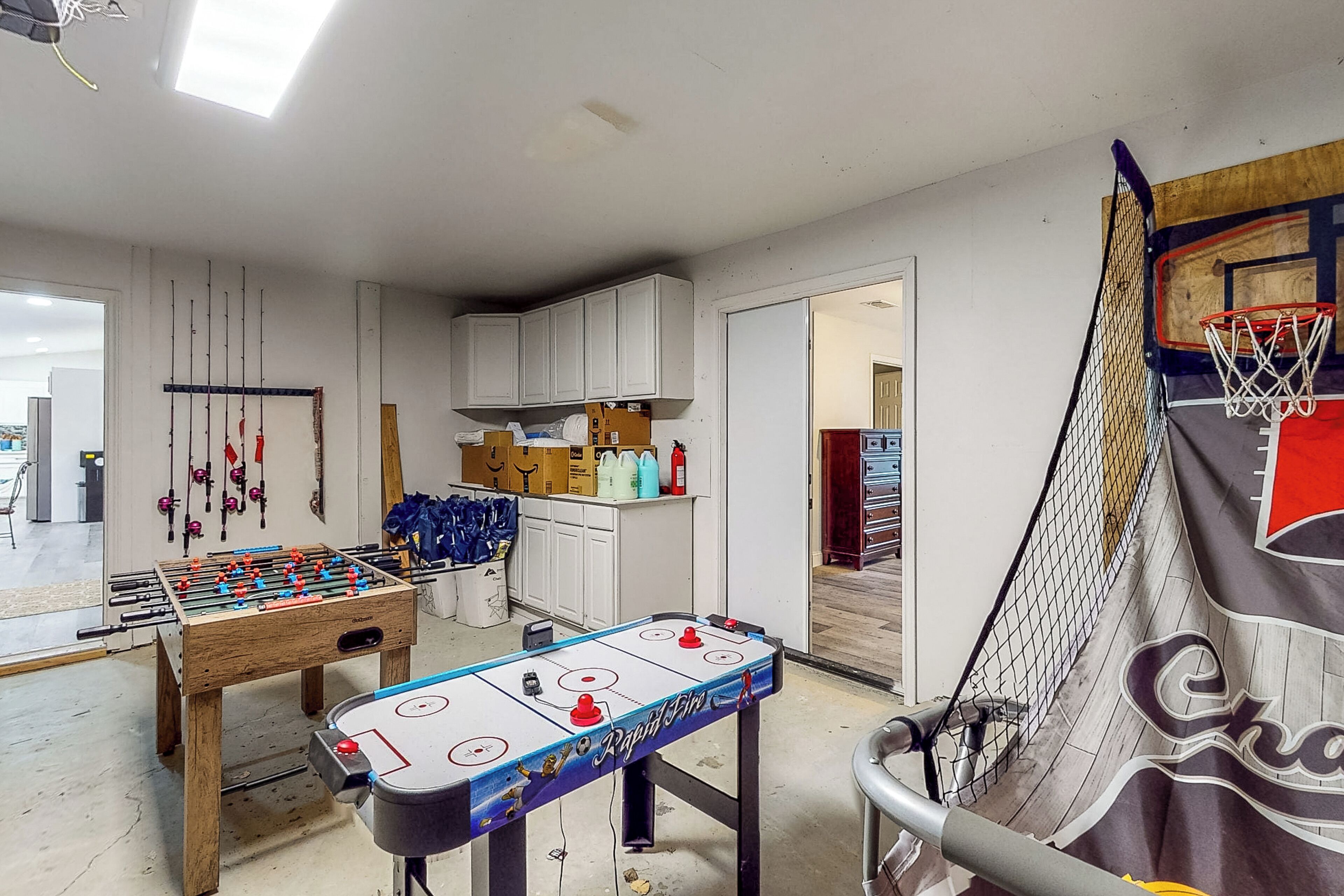 A room with two foosball tables, a basketball hoop, and a kitchenette area.