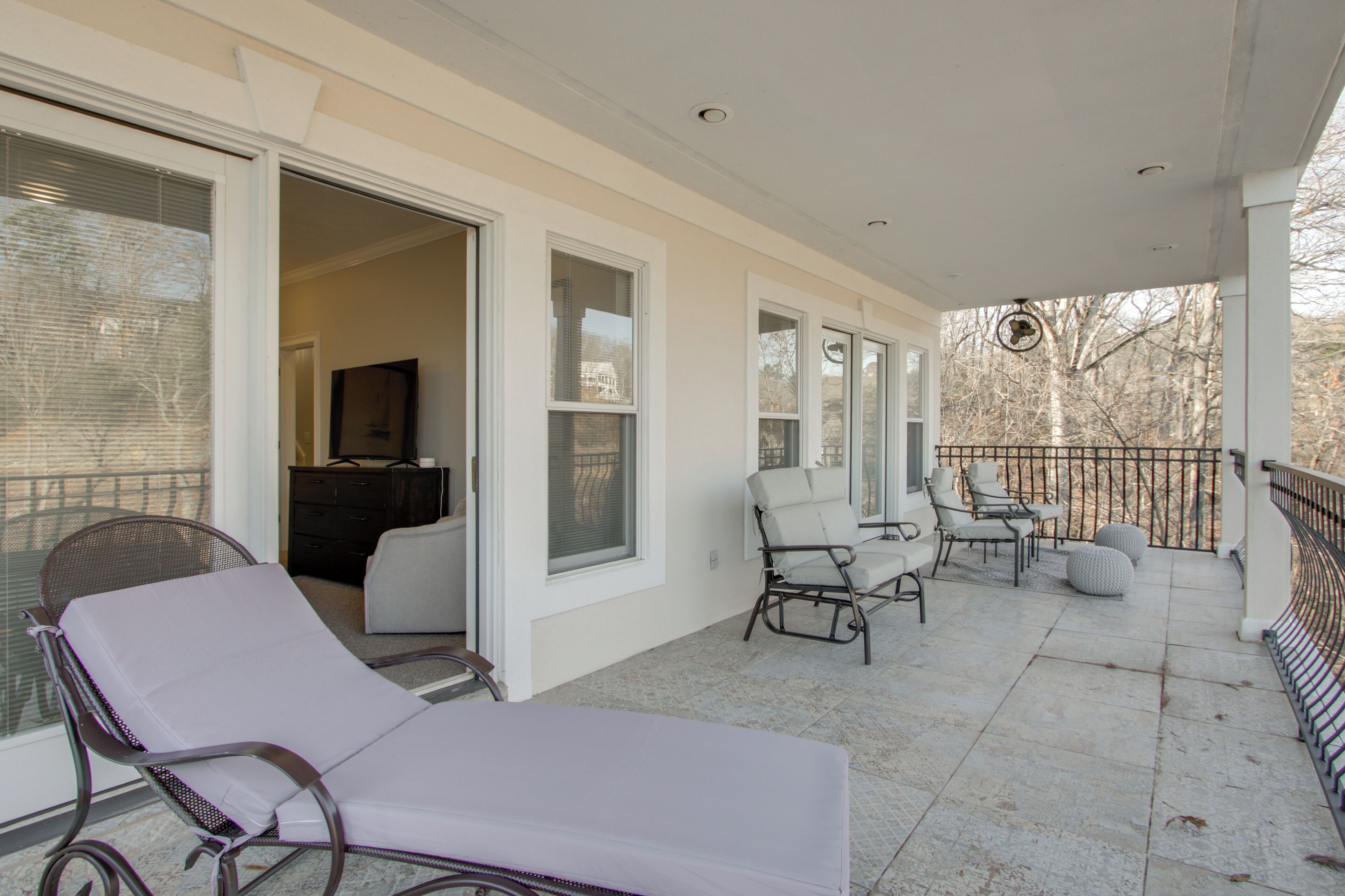 A covered outdoor area with a lounge chair, a dining table with chairs, and a view of the outdoors.