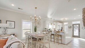 Una cocina amplia con armarios blancos, un comedor con una mesa y sillas de madera, y una sala de estar con un sofá beige.