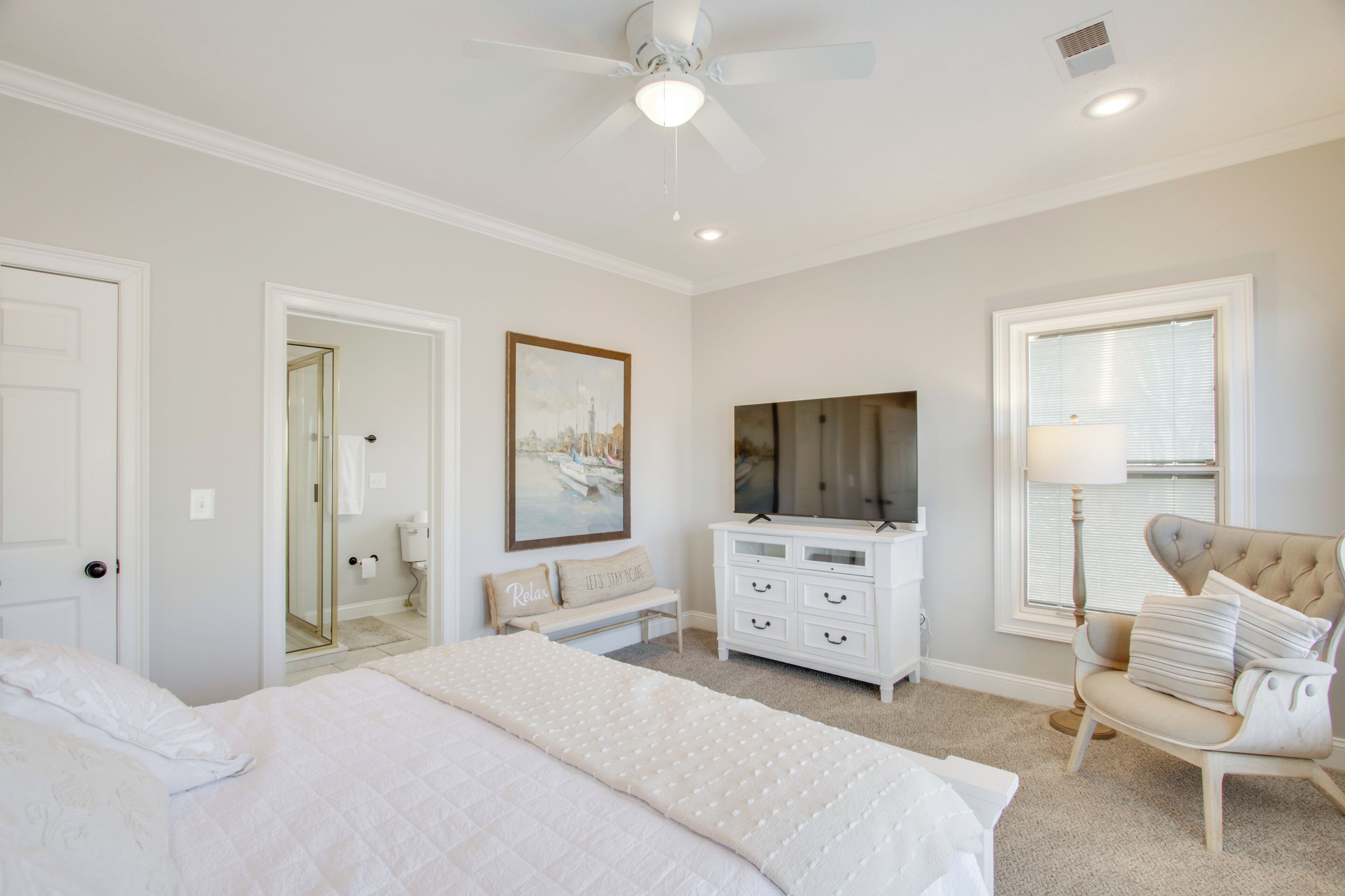 A bedroom with a bed, a dresser, a chair, a ceiling fan, and a window with blinds.