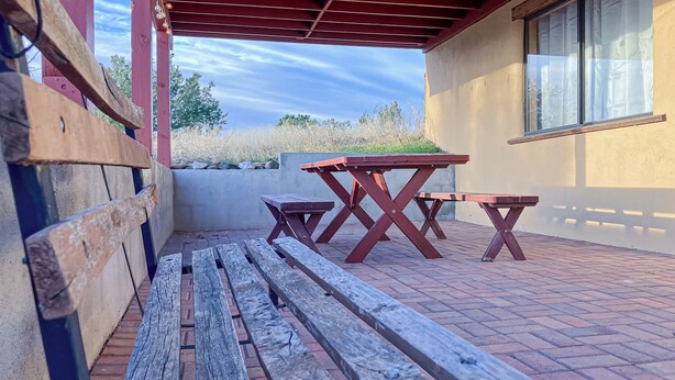 An outdoor patio with wooden benches and picnic tables, a red roof, and a view of trees and sky. - 1BR Casita w/ Mountain Views, Kitchenette, Wifi (Rimrock)