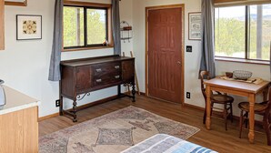 A room with a wooden dresser, a desk with a chair, a bed with a quilt, a patterned rug, and a large window with curtains. - 1BR Casita w/ Mountain Views, Kitchenette, Wifi (Rimrock)