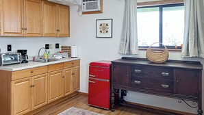 A kitchen with wooden cabinets, a red refrigerator, a dark wooden dresser, a woven basket, and a window with curtains. - 1BR Casita w/ Mountain Views, Kitchenette, Wifi (Rimrock)