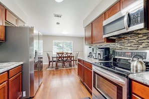 A modern kitchen with wooden cabinets, stainless steel appliances, and a dining area with a table and chairs.