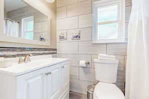 A bathroom with a white vanity, a mirror, a toilet, and a window.