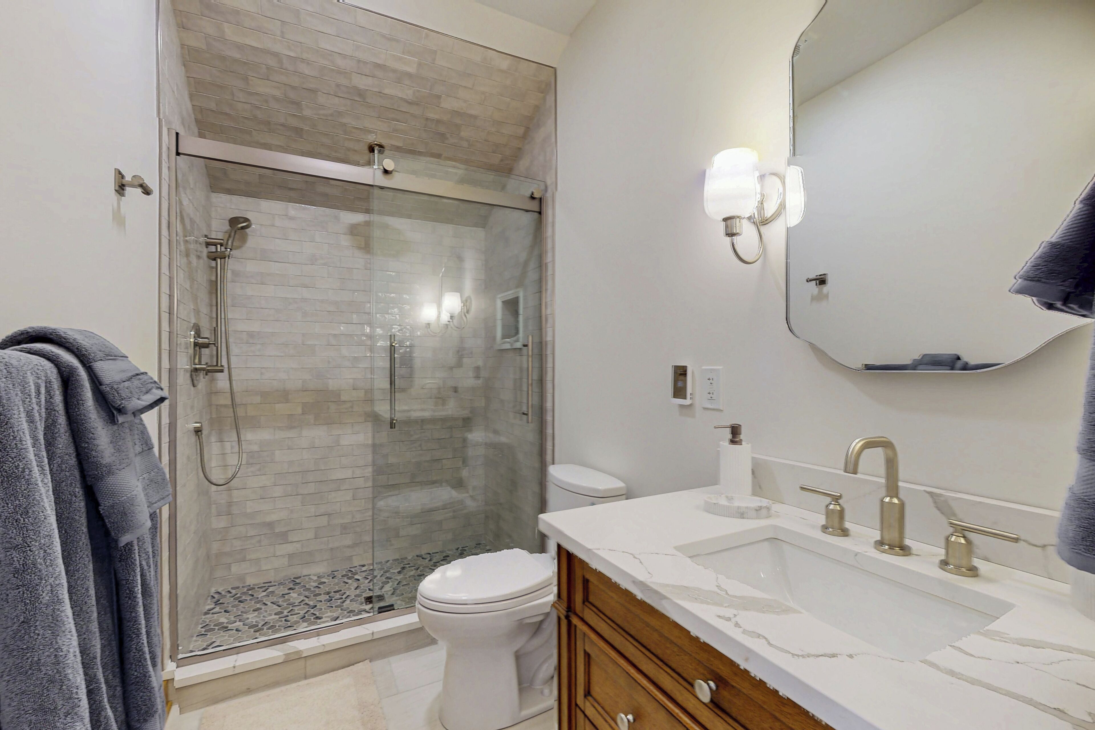 Een moderne badkamer met een douchecabine van glas, een wit toilet en een marmeren wastafel met een opbergmeubel.