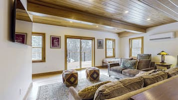 Ein geräumiges Wohnzimmer mit Holzboden, großen Fenstern, einer Sofagarnitur und einem gemusterten Teppich.