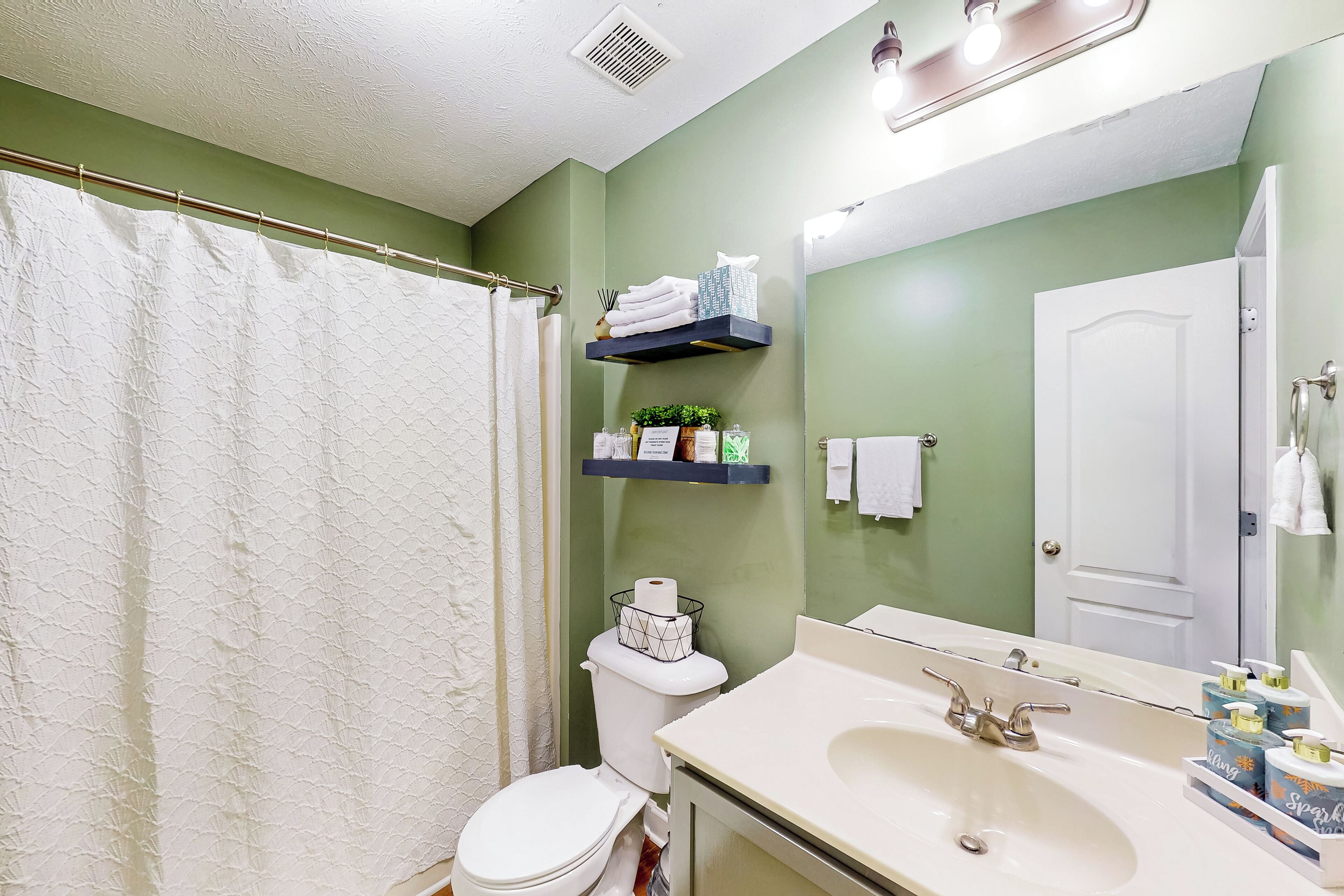 A bathroom with a shower curtain, toilet, sink, and shelves with toiletries.