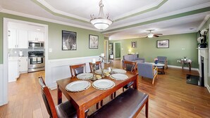 A dining room with a wooden table set for four, a chandelier, and a kitchen in the background. - Family-friendly Cameron Escape w/ Community Perks (Cameron)