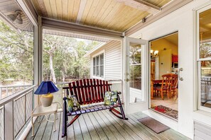 A wooden porch with a bench and a table, a door leading inside, and a view of the outdoors. - Charming Suwanee House and Bungalow! (Bell)