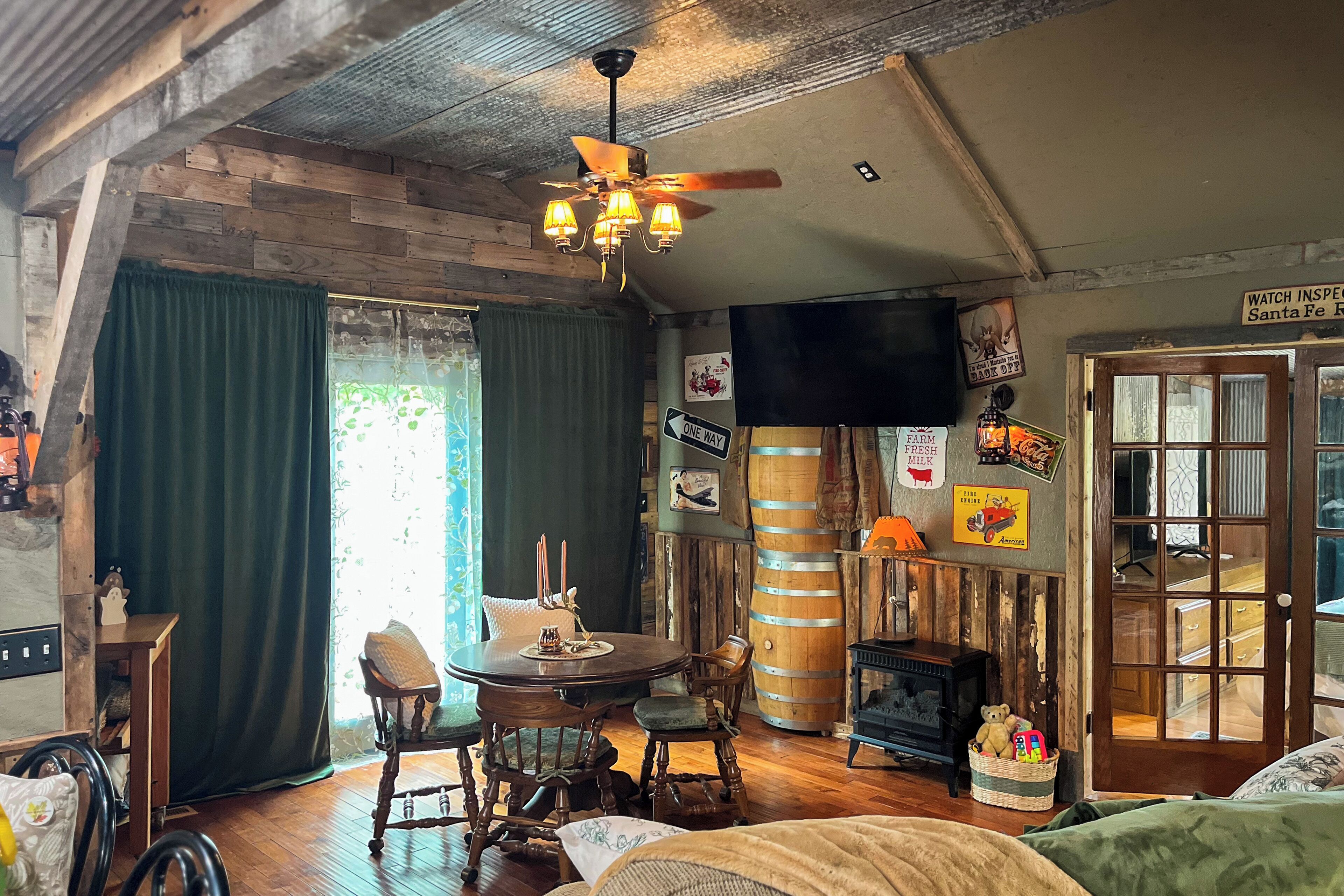Une pièce rustique avec des poutres apparentes, une table ronde entourée de chaises, un ventilateur de plafond et un téléviseur fixé au mur.