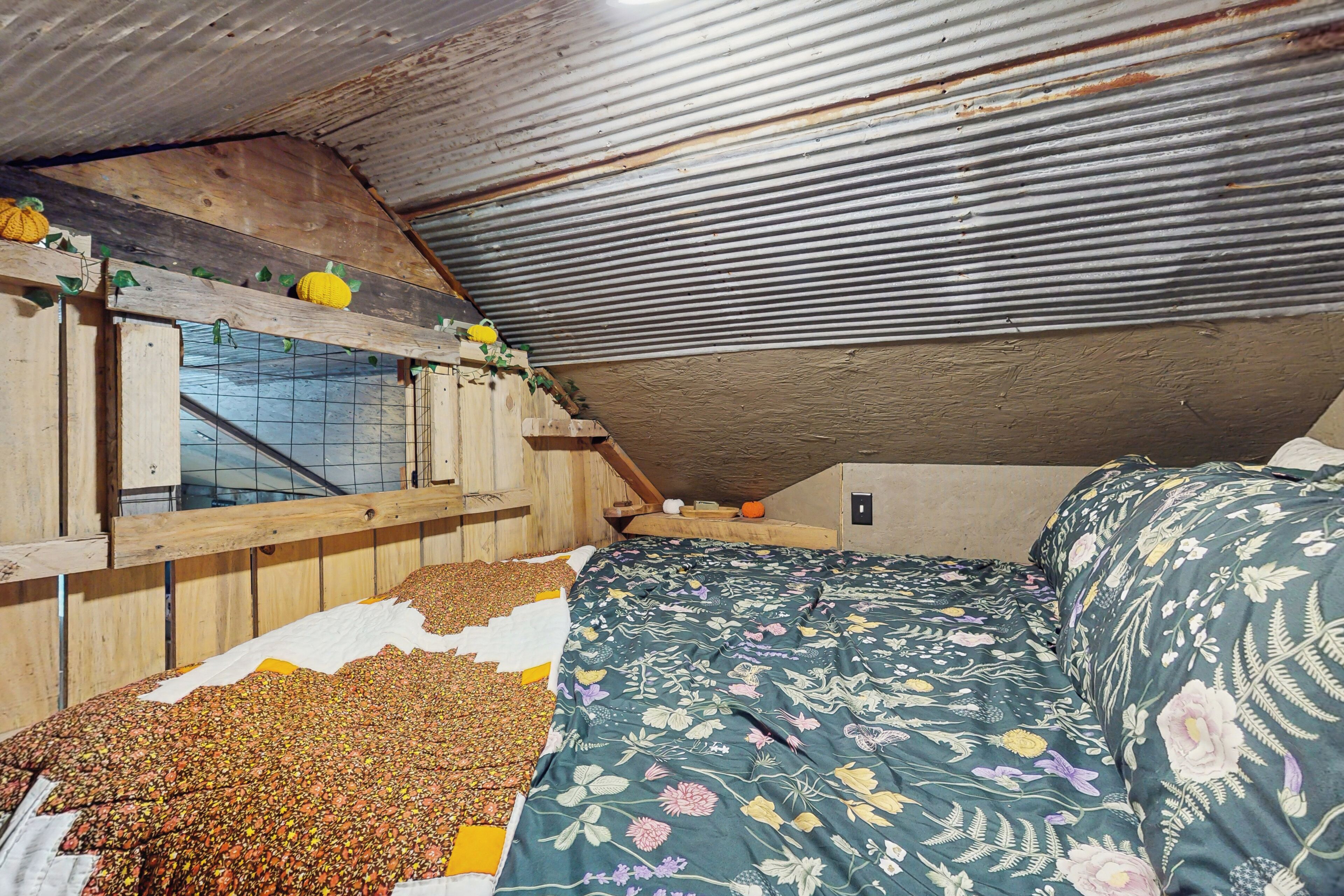 A rustic attic bedroom with a sloped ceiling, wooden beams, and a bed with floral bedding.