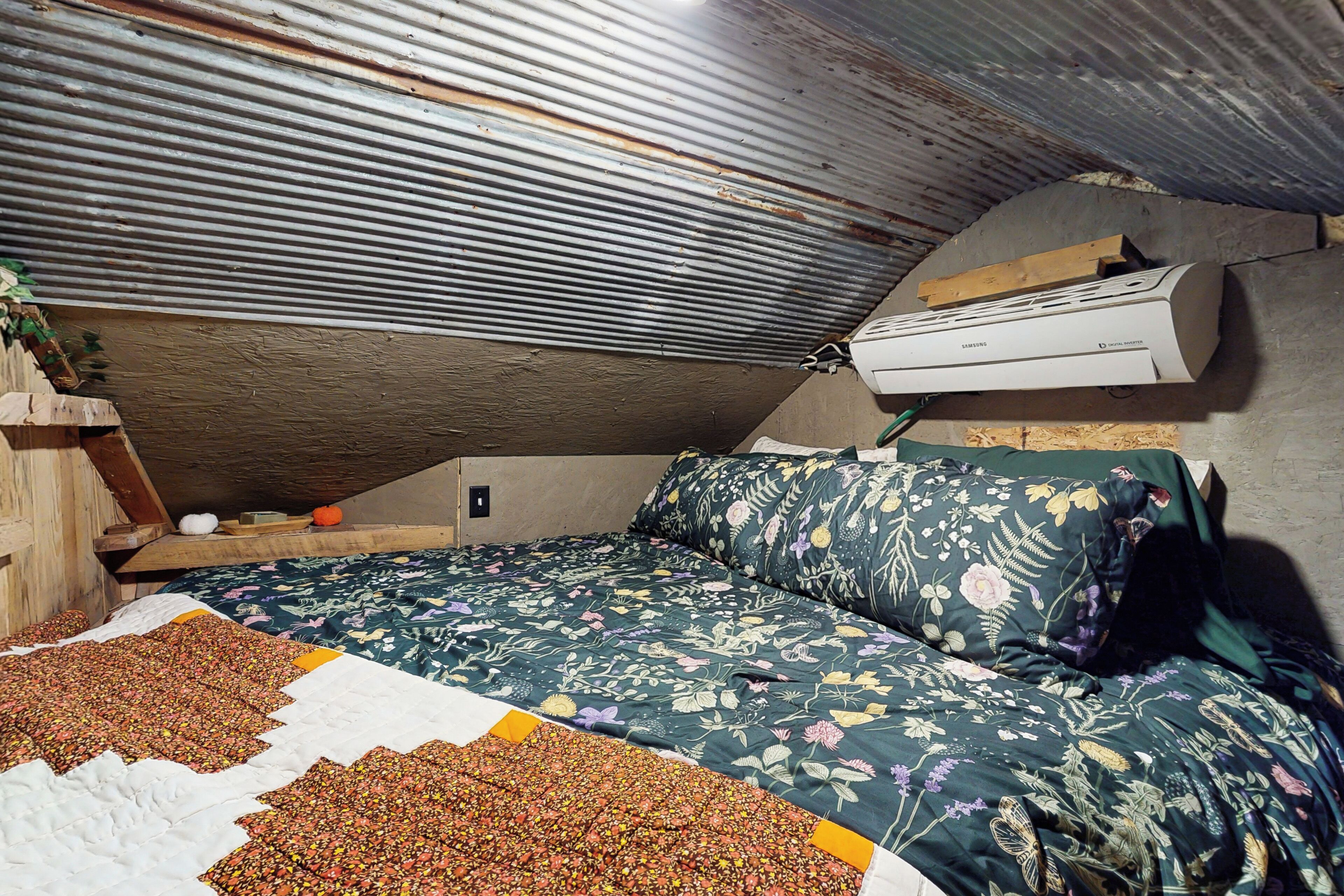 A bedroom with a sloped ceiling, a bed with floral bedding, a quilt, and a wooden headboard.
