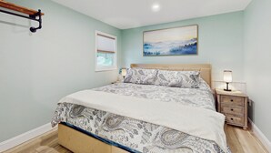A bedroom with a bed, bedside tables, a nightstand, a window, and a painting on the wall. - 2 BR Lakefront House w/ Hot Tub in ADK Park (Gloversville)