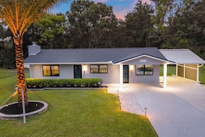 Une maison moderne de plain-pied, dotée d’un garage, d’une pelouse bien entretenue et d’un grand arbre en premier plan.