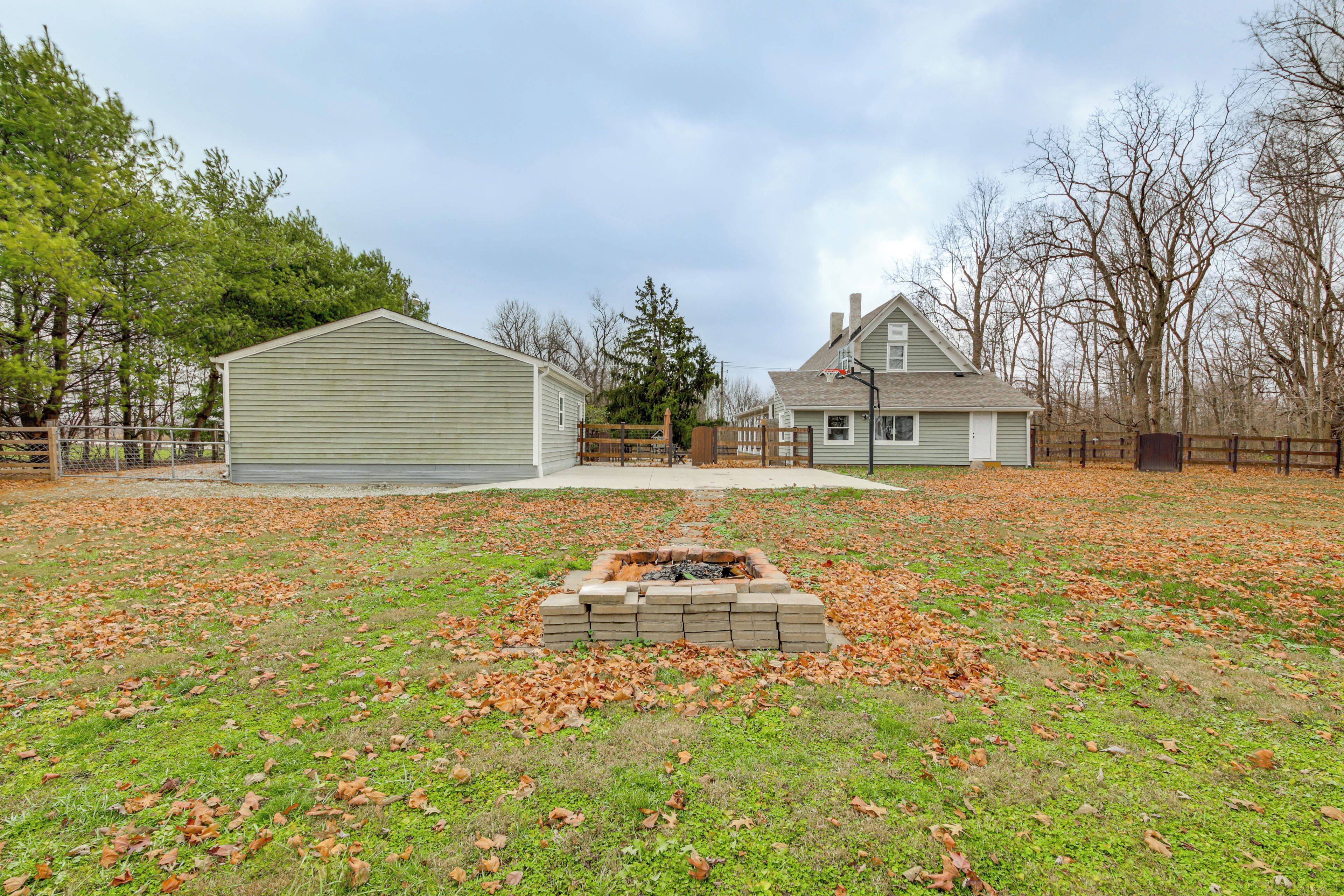A residential area with two houses, a fenced yard, and a fire pit.