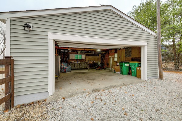 A garage with a gravel driveway, wooden fence, and a utility box on the wall. - Zionsville Winter Stay: Fire Pit & Big Yard (Zionsville)