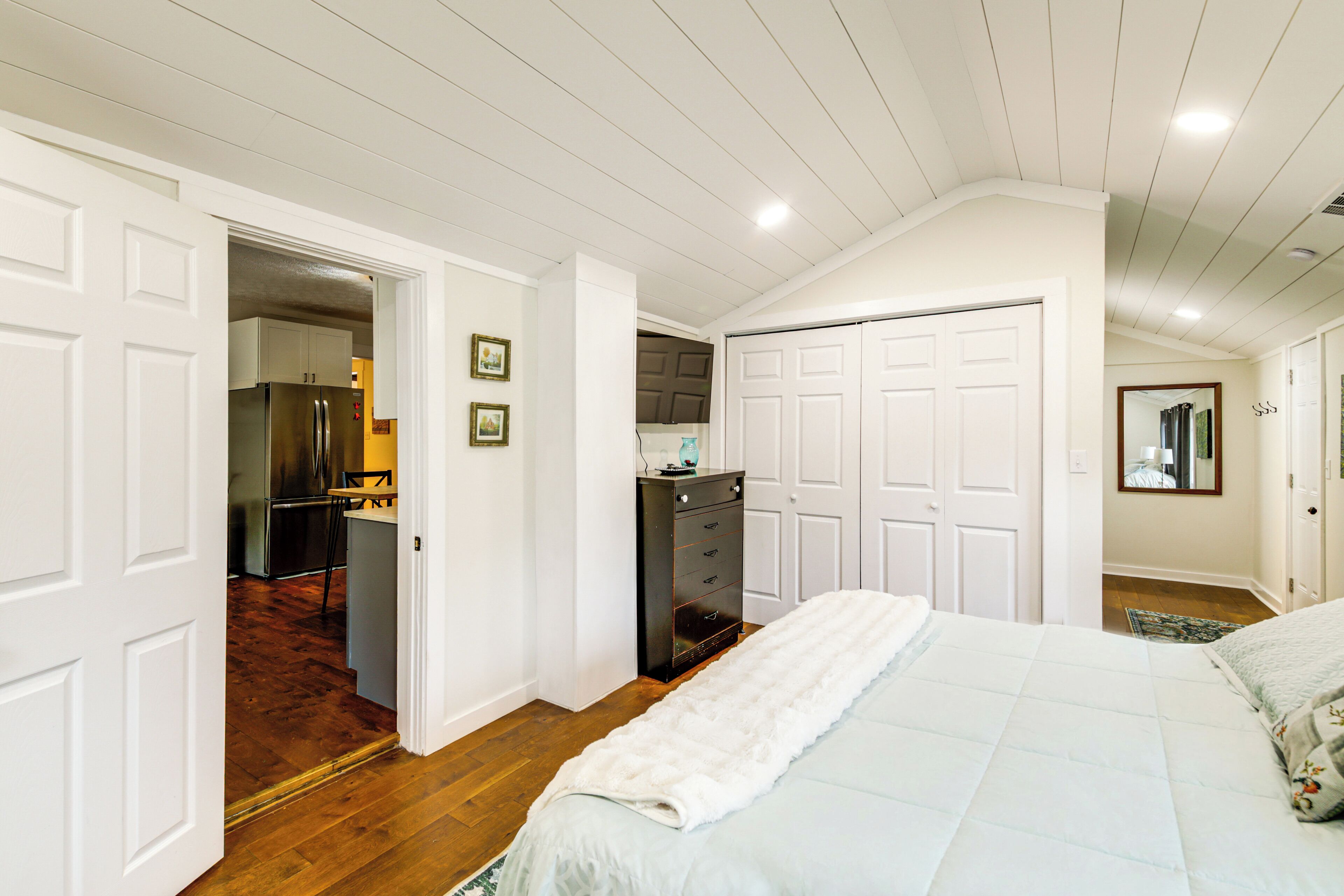 A bedroom with a bed, a dresser, a closet, and a doorway leading to a kitchen.