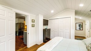 Un dormitorio con una cama, un aparador, un armario y una puerta que da a una cocina.