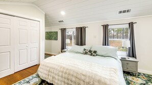 Un dormitorio con una cama grande, una mesita de noche, un aparador y una ventana con cortinas.