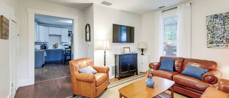 A living room with a brown leather sofa, a wooden coffee table, and a leather armchair. There is a television mounted on the wall and a fireplace.