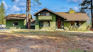 A two-story wooden house with a green exterior, a front porch, and a chimney. - 3BR Rustic Riverfront Home w/ Wood Stove (Blairsden-Graeagle)