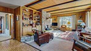 A cozy living room with a stone fireplace, leather furniture, and wooden paneling. - 3BR Rustic Riverfront Home w/ Wood Stove (Blairsden-Graeagle)