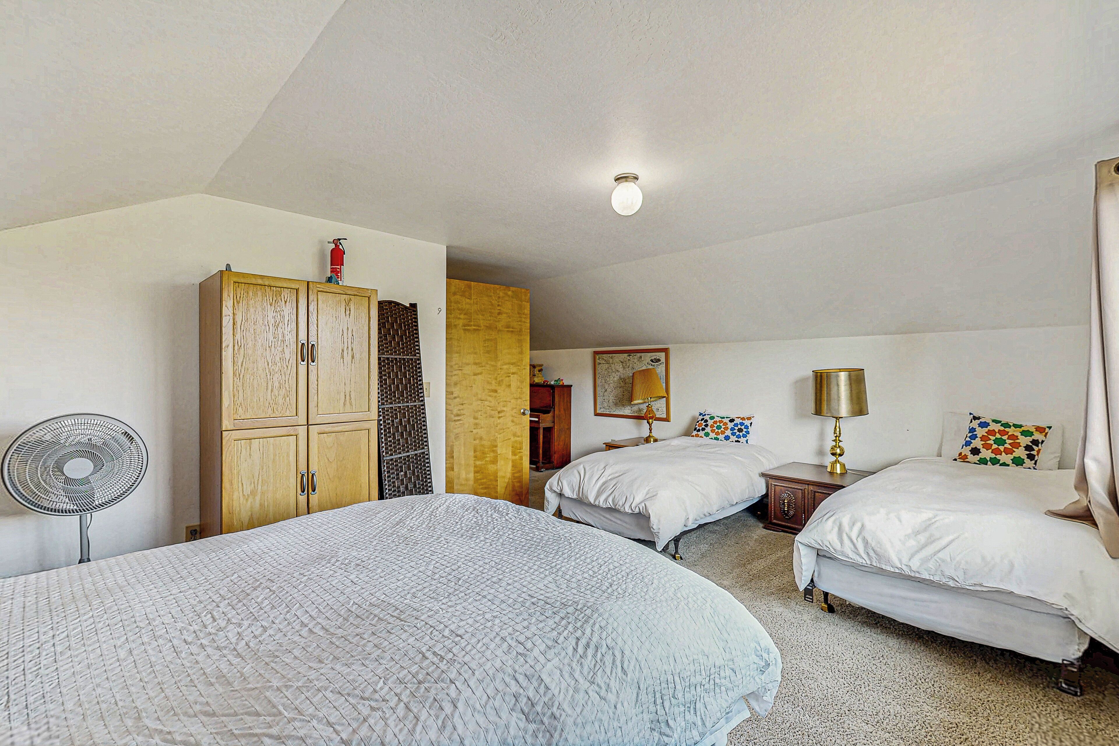 A bedroom with two beds, a wooden wardrobe, a fan, and a ceiling light.