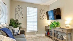 A living room with a sofa, a television mounted on the wall, and a console table with a plant. - Endless Entertainment! Unique & Cozy Theodore Home (Theodore)