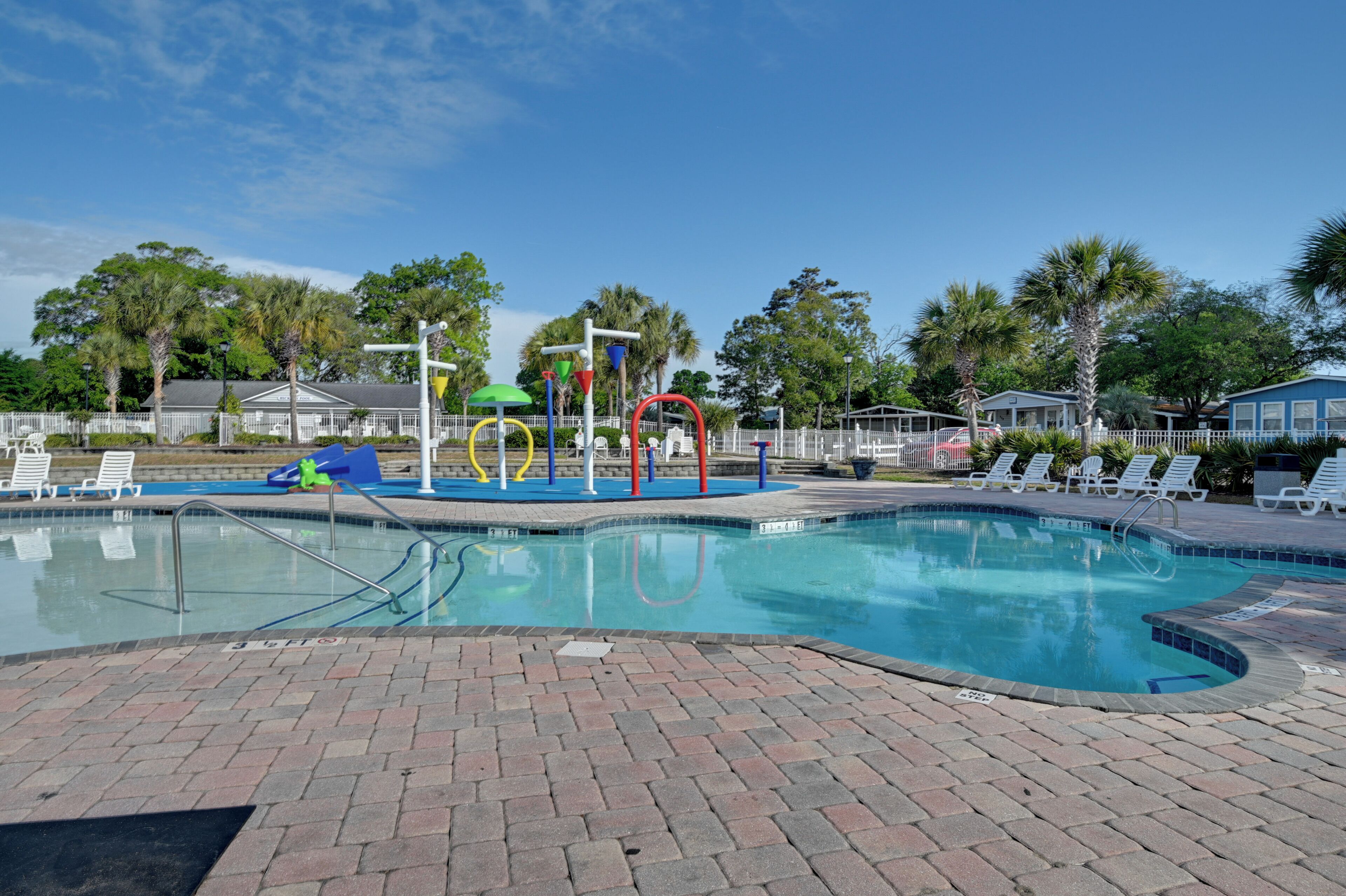 Piscina con borde de ladrillo, rodeada de sillas de descanso y palmeras.