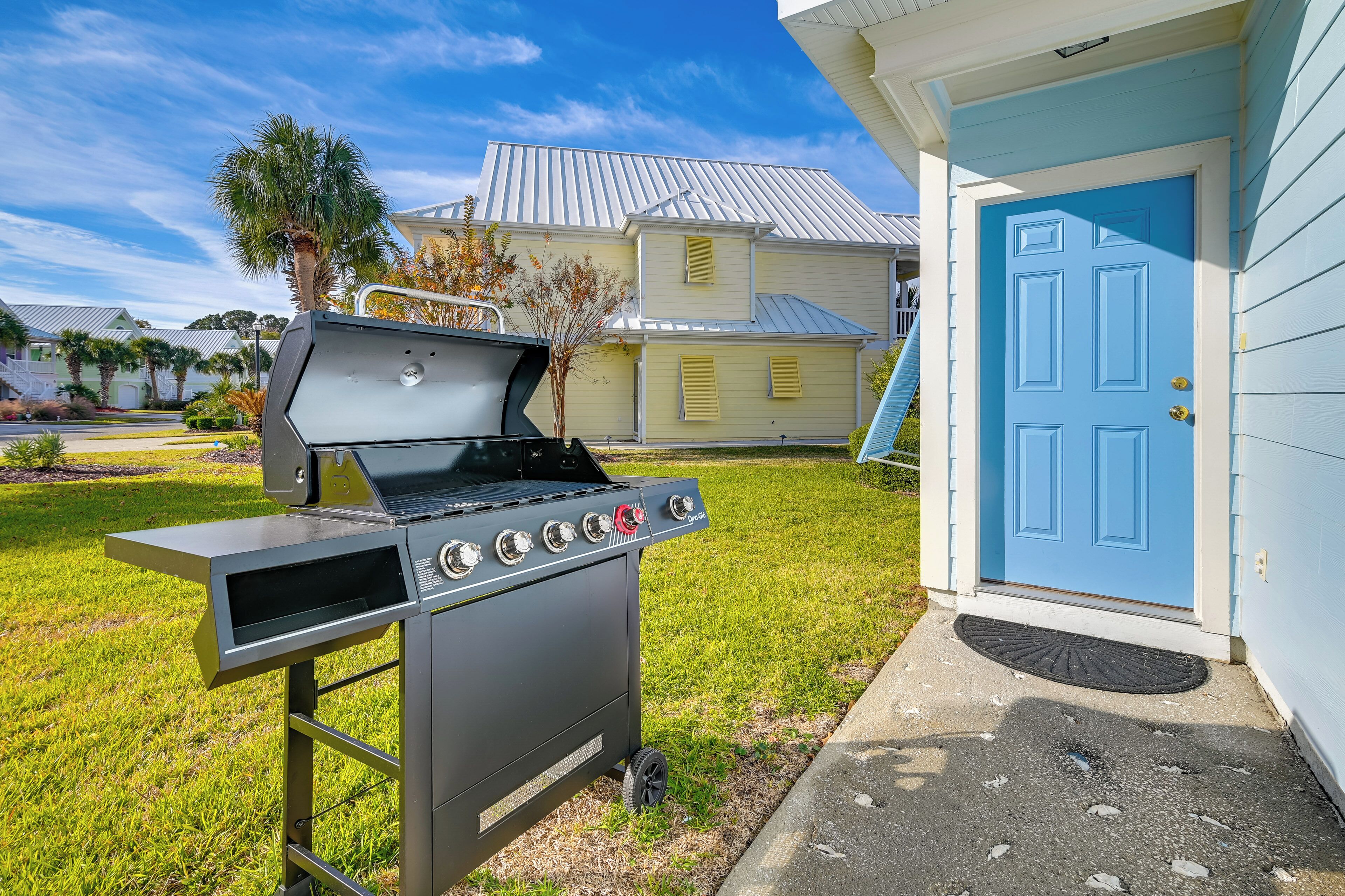 A portable grill in a grassy yard with a blue door and a house in the background.