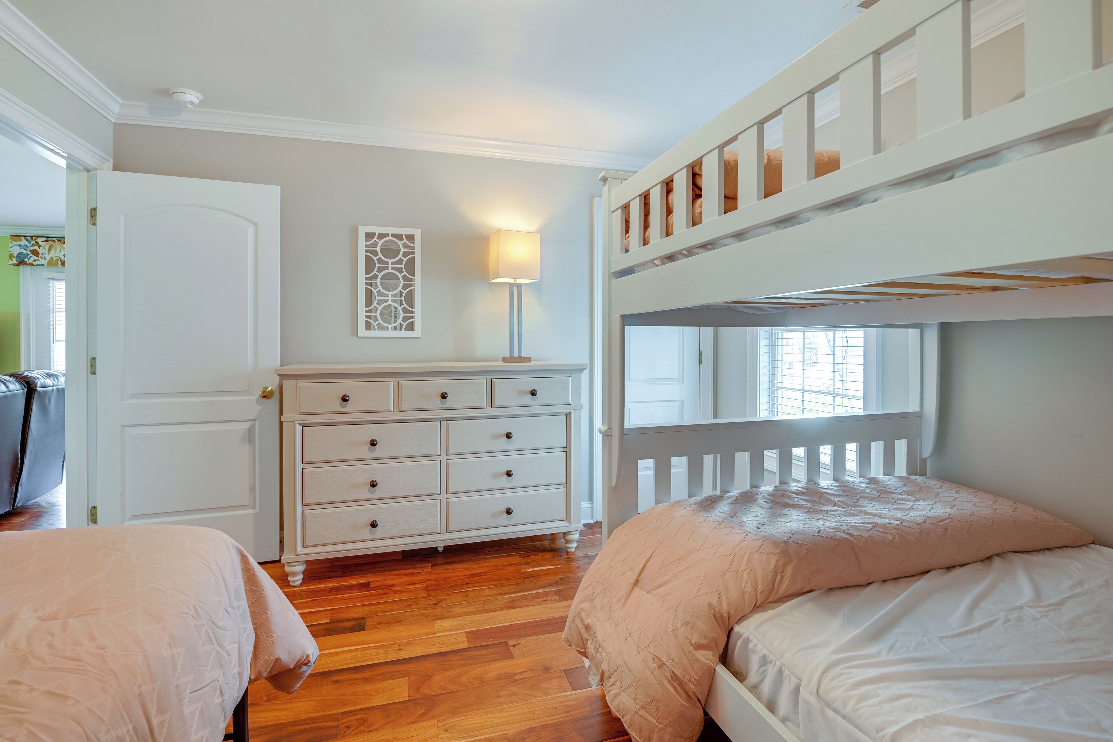 Une chambre à coucher avec un lit superposé, une commode, une lampe et une fenêtre.