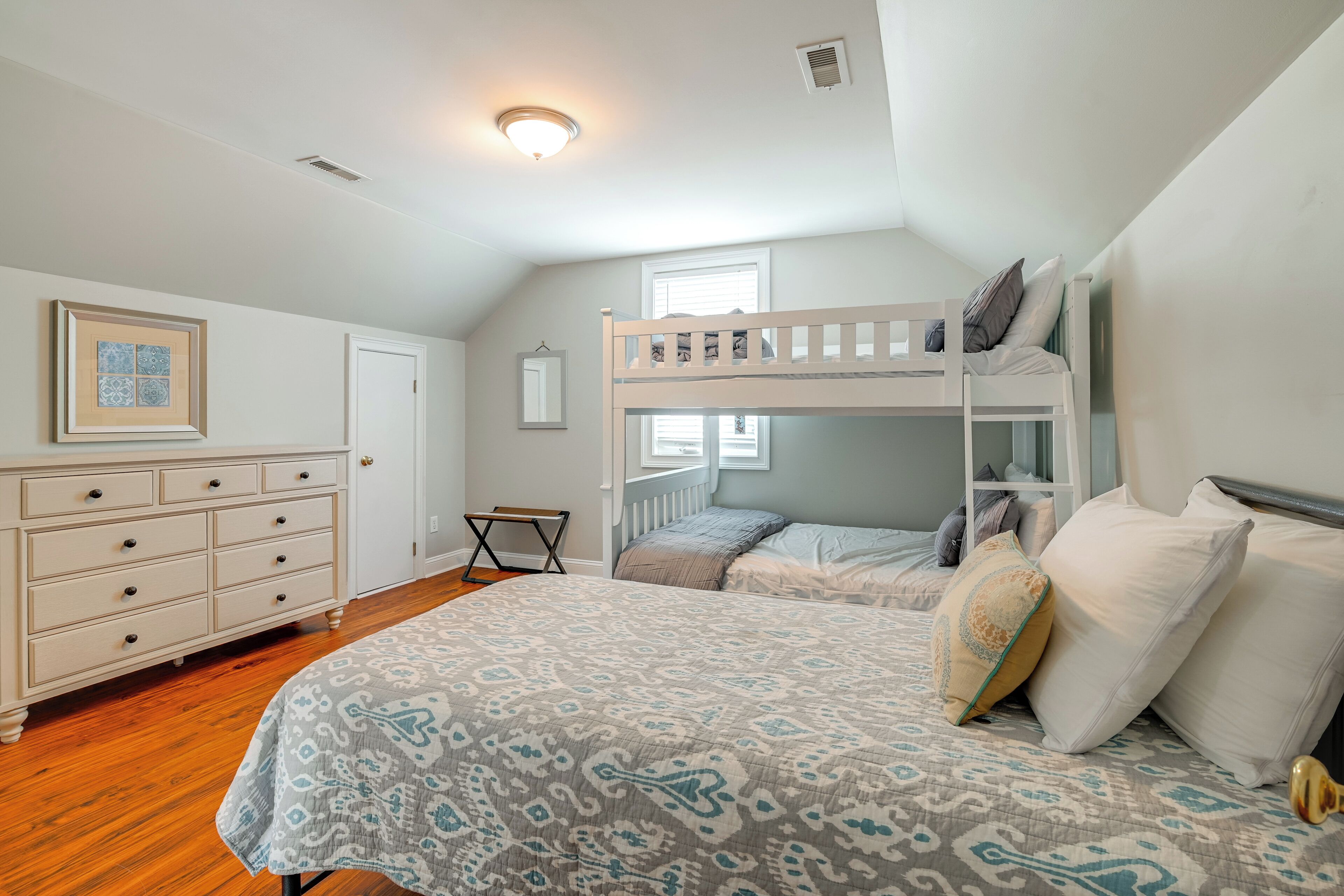 A bedroom with a bunk bed, a dresser, a patterned bedspread, and a small table.