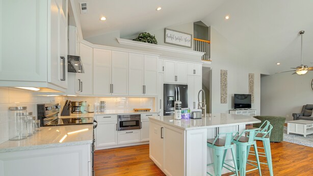 Una cocina moderna con armarios blancos, una isla central con taburetes y horno empotrado, además de un refrigerador.