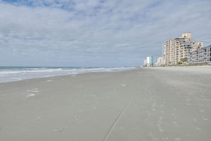 A beach with a sandy shore, ocean waves, and buildings in the background. - Spacious Home w/ Oceanside Village Resort Perks! (Murrells Inlet)