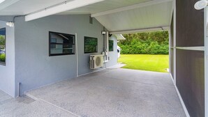 Un espacio al aire libre techado, con piso de concreto, una unidad de aire acondicionado y vistas a un césped verde.