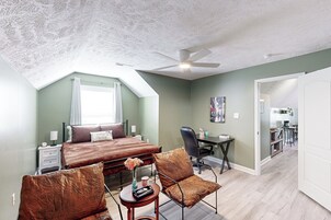 A bedroom with a bed, two chairs, a desk, and a ceiling fan.