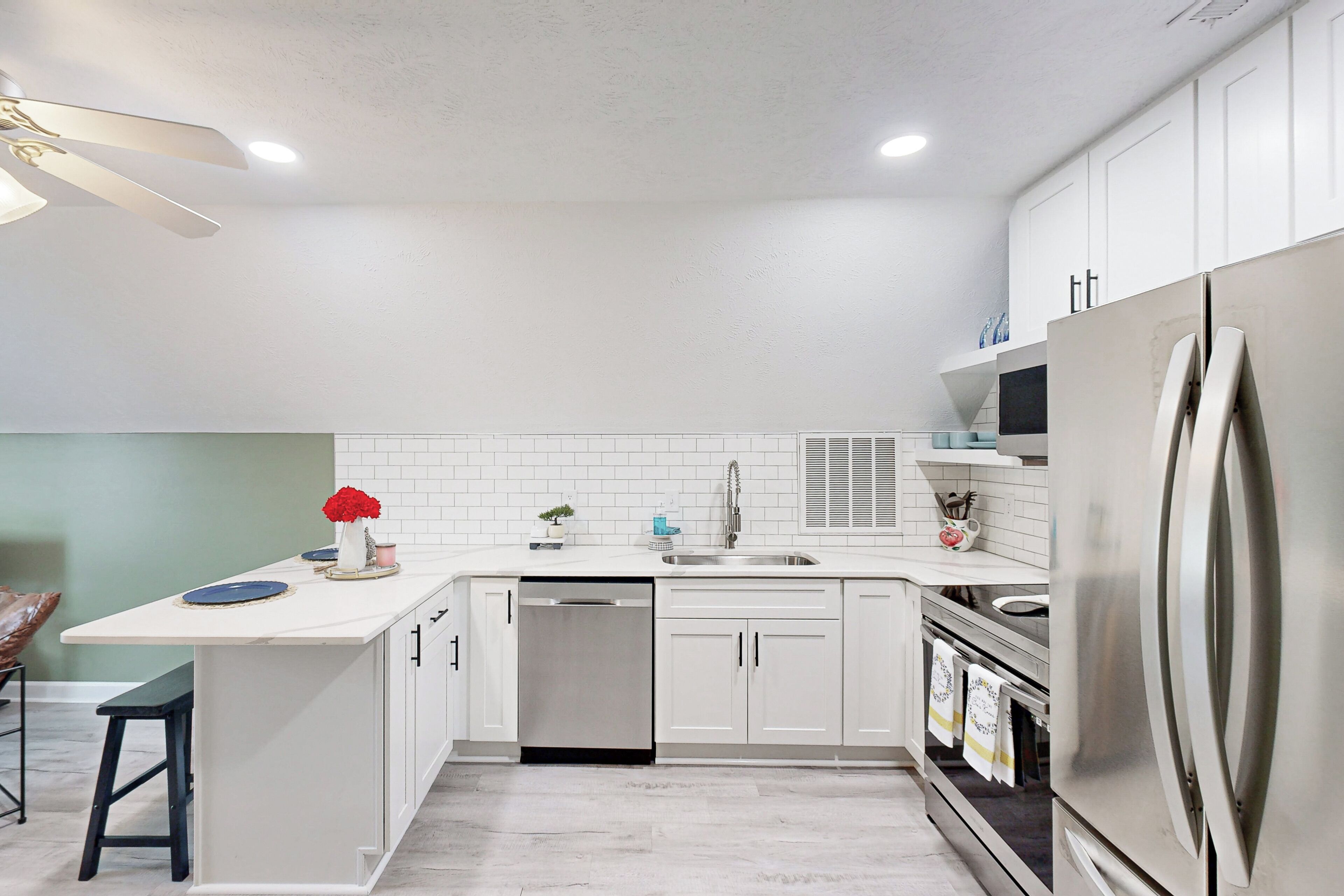 Una cocina moderna con armarios blancos, un refrigerador de acero inoxidable, lavavajillas y un taburete de bar.