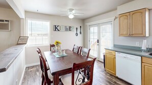 A dining area with a wooden table and chairs, a ceiling fan, and a kitchen with wooden cabinets and a dishwasher. - History, Hikes & Cozy Nights: Parowan Gem w/ Deck! (Parowan)