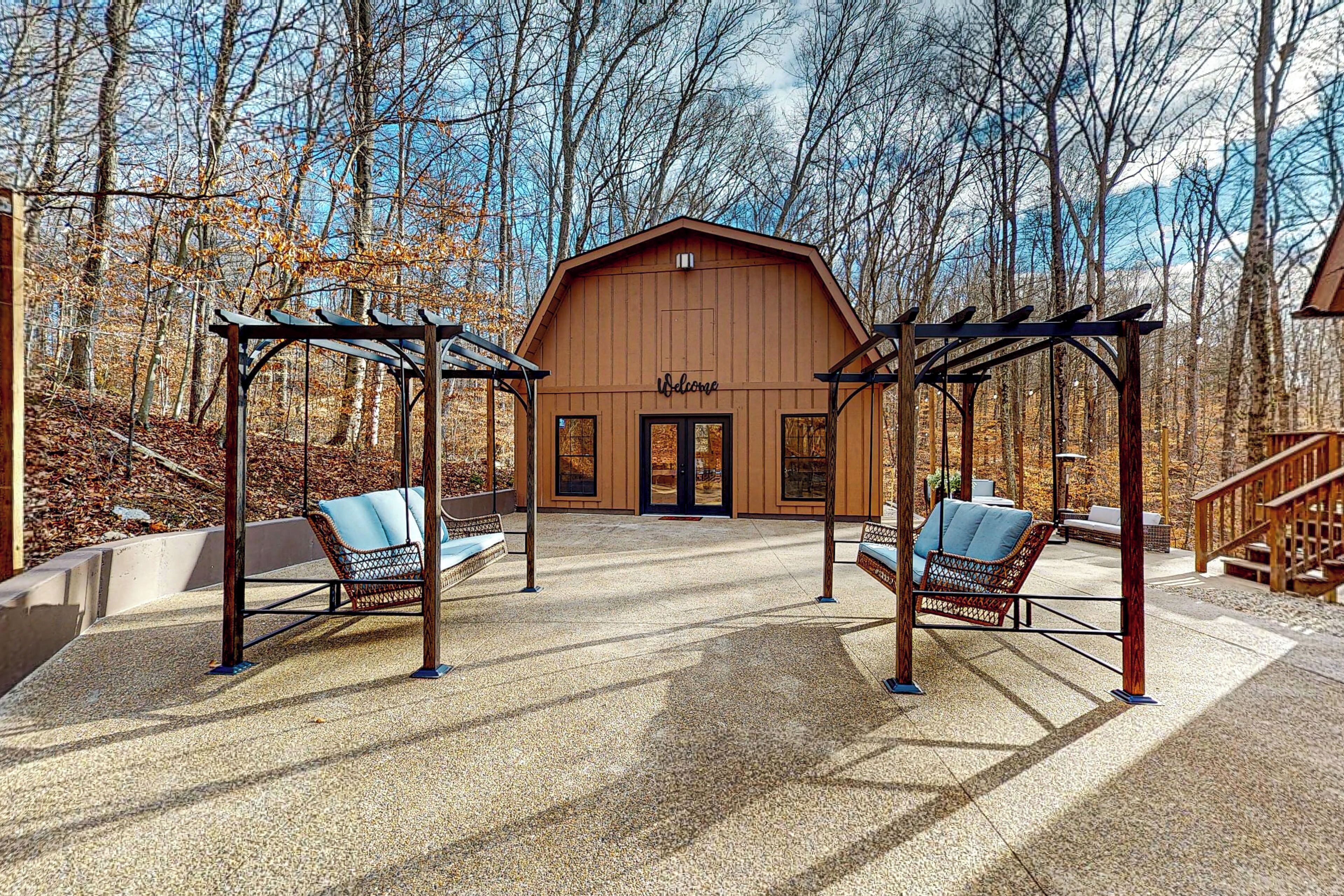 Une grange en bois avec une pancarte « Bienvenue », deux chaises suspendues et une terrasse en béton.