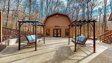 Une grange en bois avec une pancarte « Bienvenue », deux chaises suspendues et une terrasse en béton.