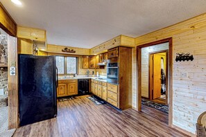 A modern kitchen with wooden cabinetry, a black refrigerator, and a built-in oven. - Hot Tub & Fire Pit: Wooded Indiana Escape (Columbus)