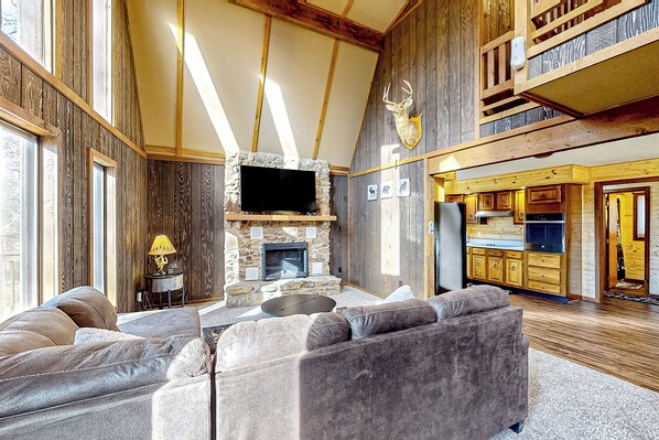 A spacious living room with a stone fireplace, a large flat-screen TV, and a cozy seating area. - Hot Tub & Fire Pit: Wooded Indiana Escape (Columbus)