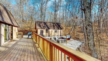 Une terrasse en bois avec des sièges d’extérieur et une vue sur un chalet entouré d’arbres.